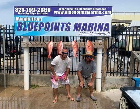 Two men pose in front of the Bluepoints Marina sign