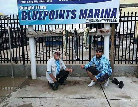 Two men pose below Bluepoints Marina sign