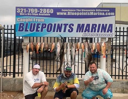 Three fishermen posing below the Bluepoints Marina sign